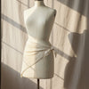 Mannequin wearing a white triangular scar with lace details against a textured wall.