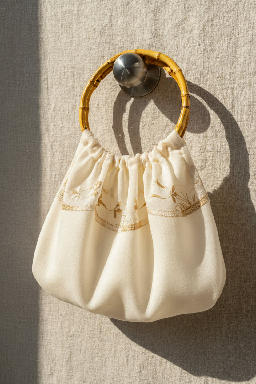 Small cream-colored handbag with a wooden handle on a textured beige background